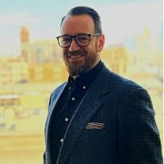 Dwayne Huffman NFL Draft Photo A Caucasian male with glasses and a beard, dressed in a suit coat, smiles with downtown KC seen behind him