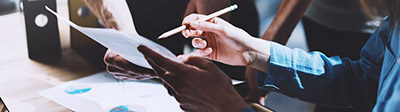Close up of a person holding a page of paper and pointing to it with a pencil